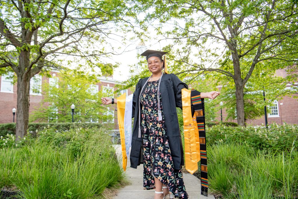 Tiana shows off her graduation cords and stoles in a garden.