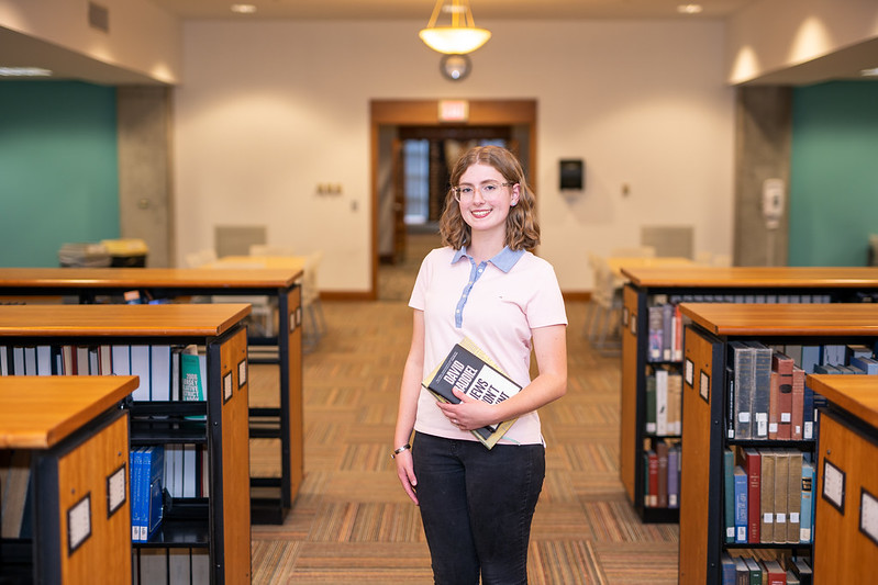 Kathryn holds a textbook inside Campbell Library.