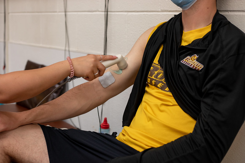 Close-up of Samantha Santos using an ultrasound machine on a baseball player's arm for active physical therapy.