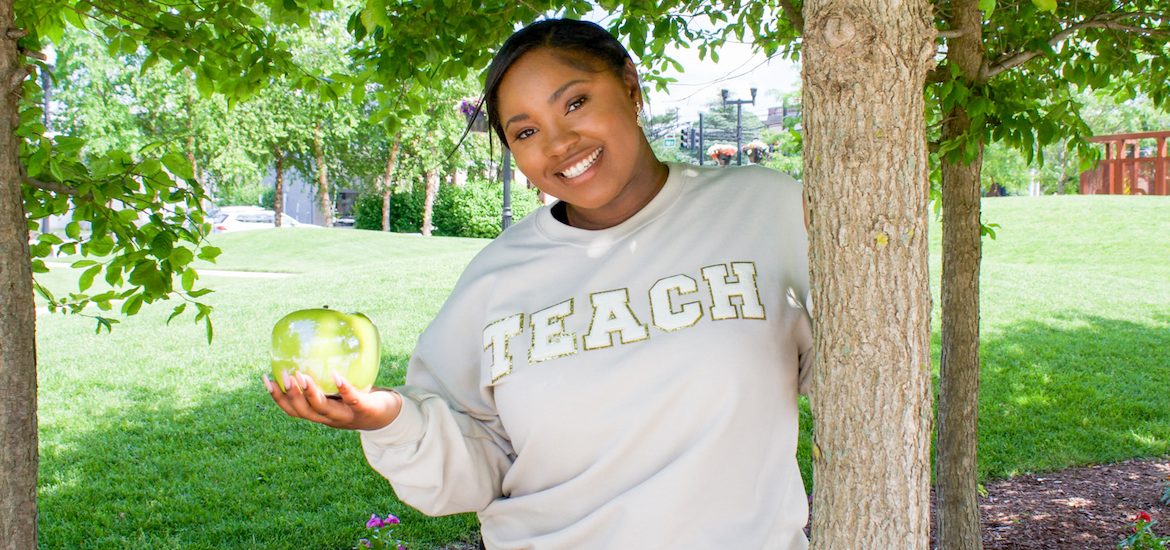 Mariah holds an apple while standing outside on campus.
