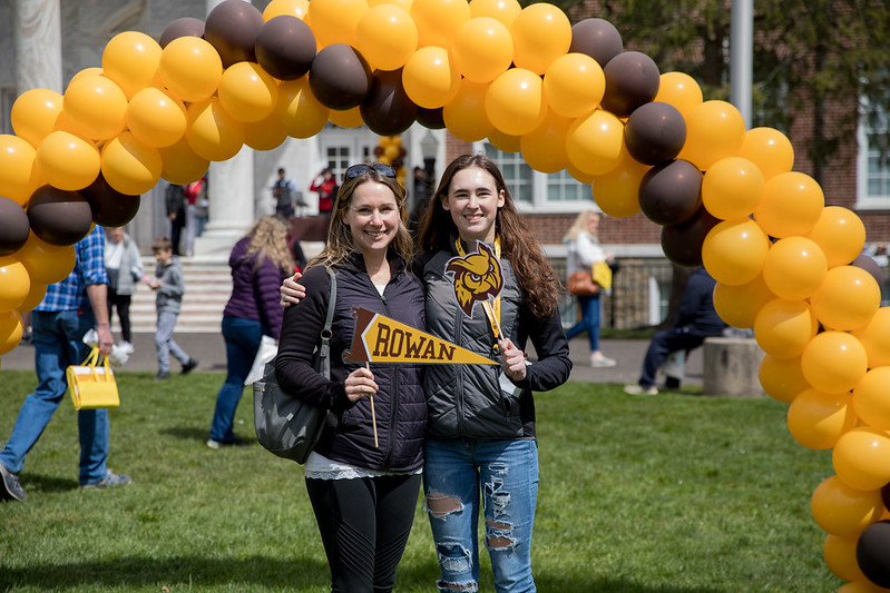 An accepted student is posing with her mother in front of the balloon archway.