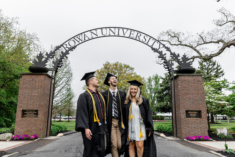 Nick, left, laughs with his friends in their graduation attire under the Rowan arch.