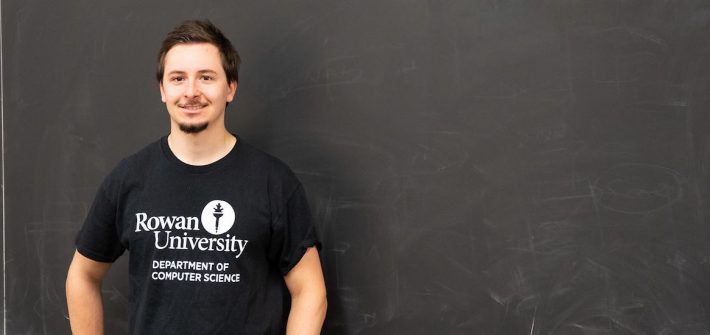 Jon stands in front of a chalkboard inside a a classroom on campus.