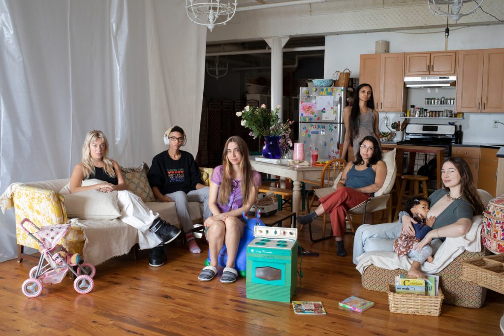 Seven people in a shared living area, photographed for New York Times magazine.