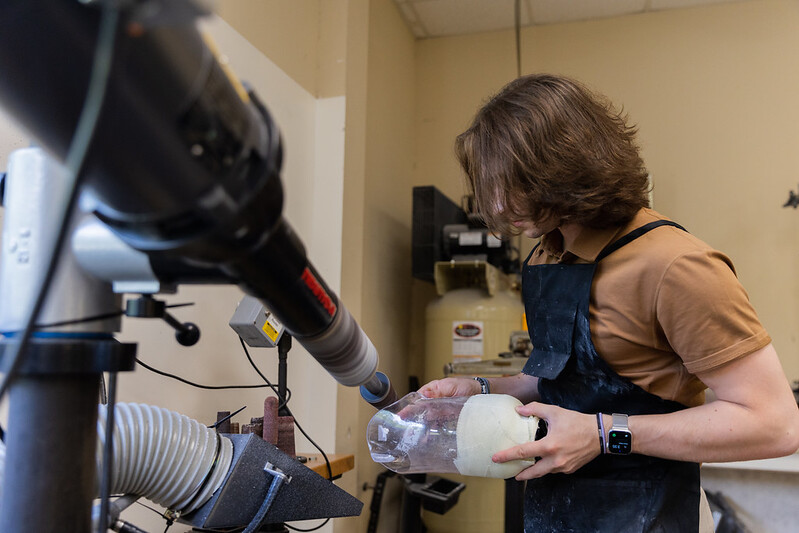 Dominic sands a prosthetic with a machine.