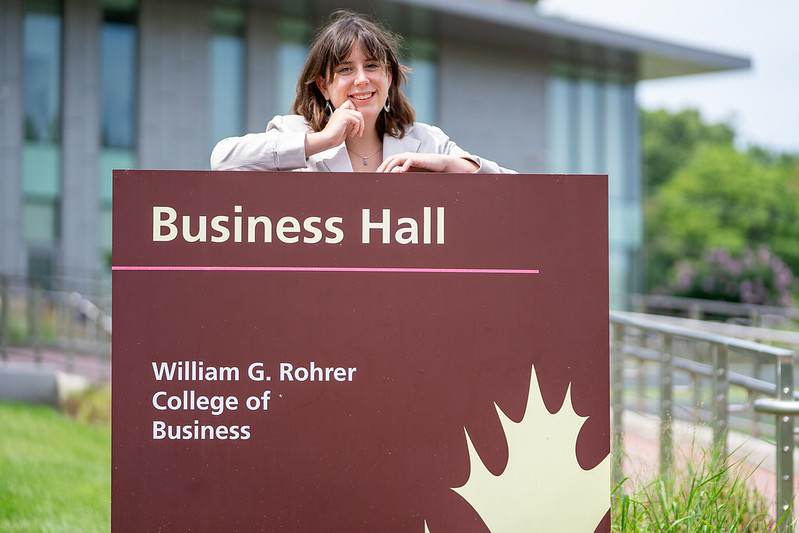 Annabella is leaning on the Business Hall sign and smiling. 