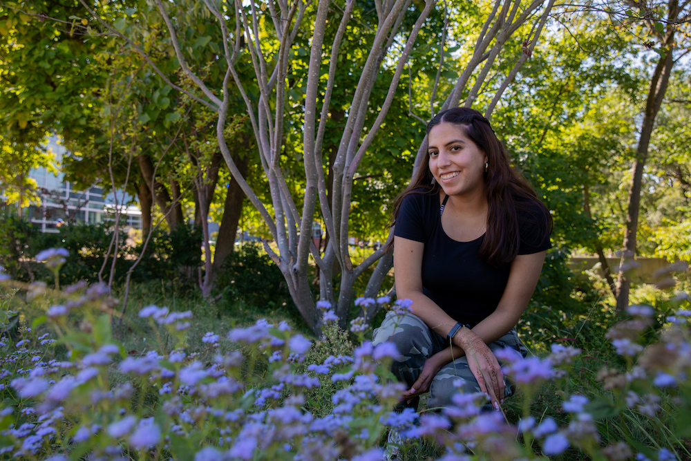 Angelica poses in front of purple flowers on campus.