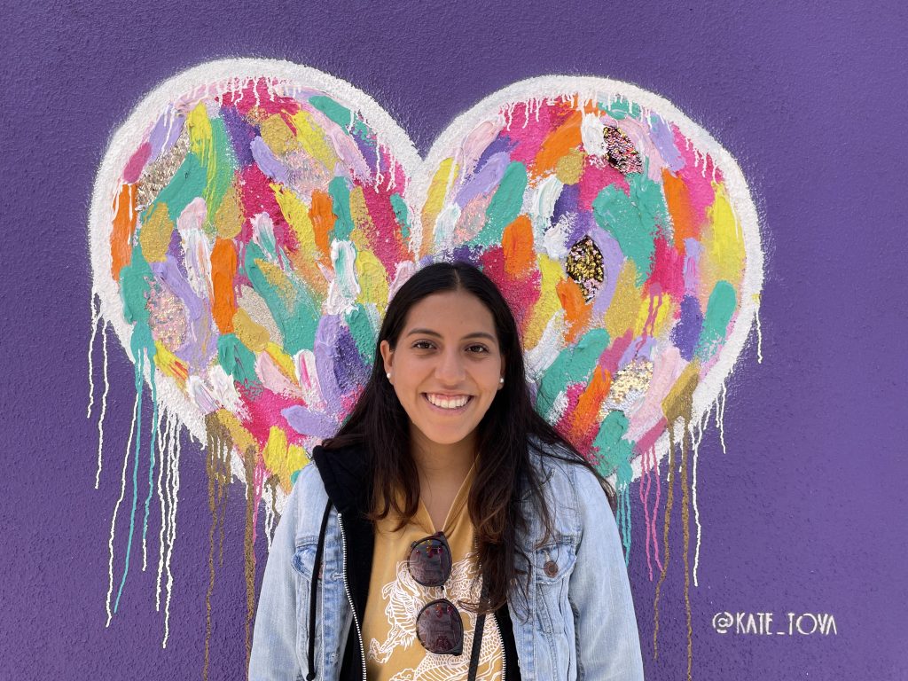 Angelica smiles in front of a colorful heart mural.