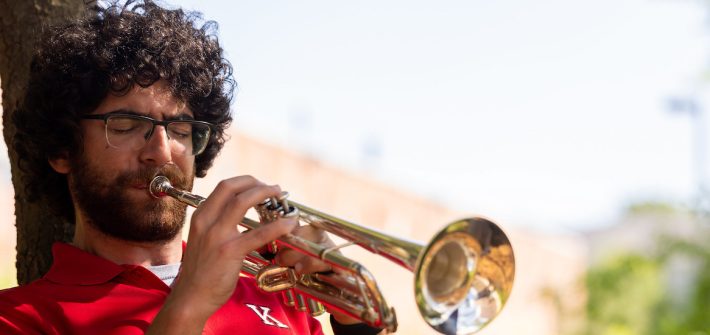 Music education alumnus Mike Massaro plays the trumpet wearing a red polo shirt.