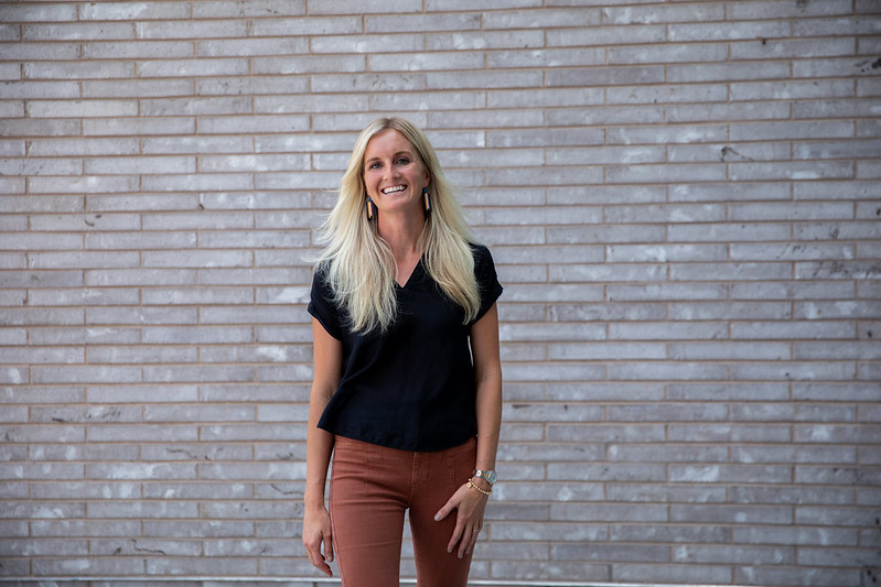 Katrina is standing in front of a brick wall and smiling outside Discovery Hall.