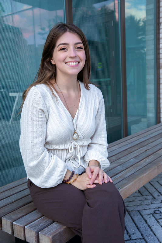 Rowan University Supply Chain and Logistics major Alivia sits on a bench in front of Discovery Hall.