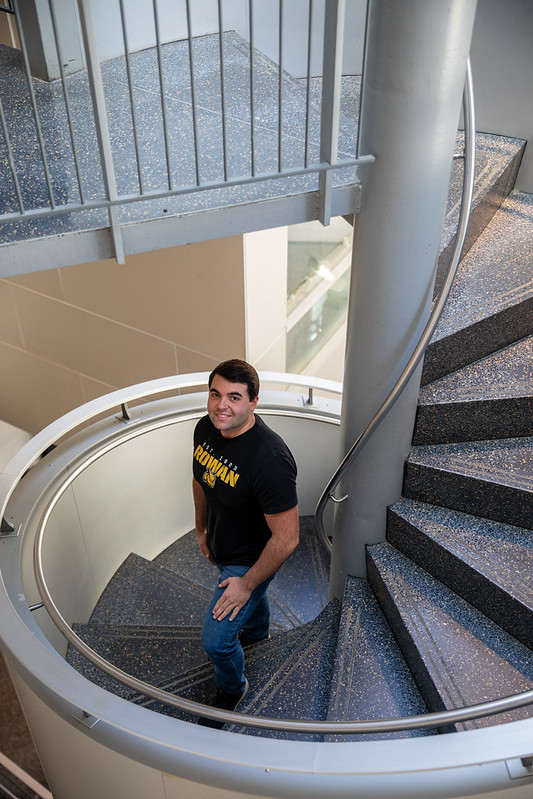 Mechanical Engineering major Carmine stands on the stairs inside Rowan Hall.