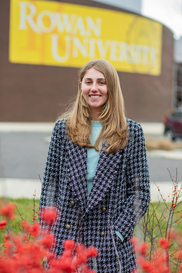 College of Education student Isabella poses outside in front of a large Rowan University sign. 
