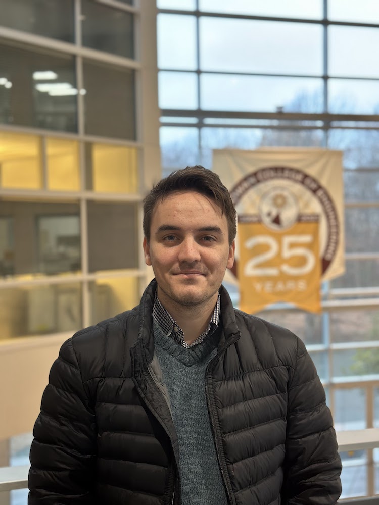 Electrical and Computer Engineering major Benjamin Busler stands in front of a banner inside Rowan Hall.