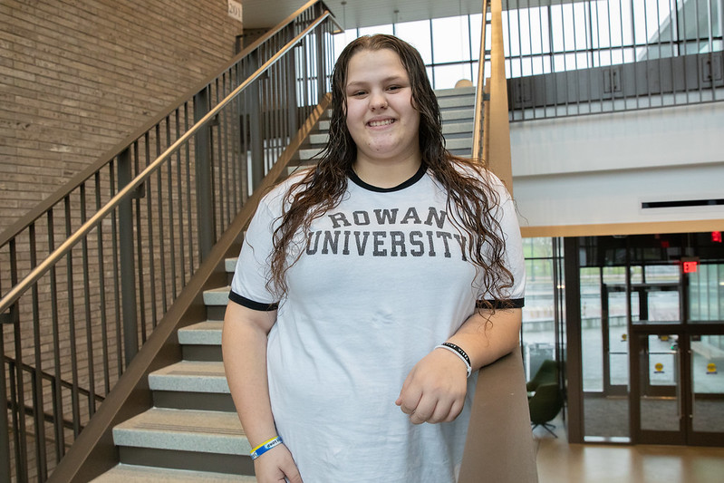 Laynie smiles and stands inside Discovery Hall wearing a white Rowan University t-shirt.