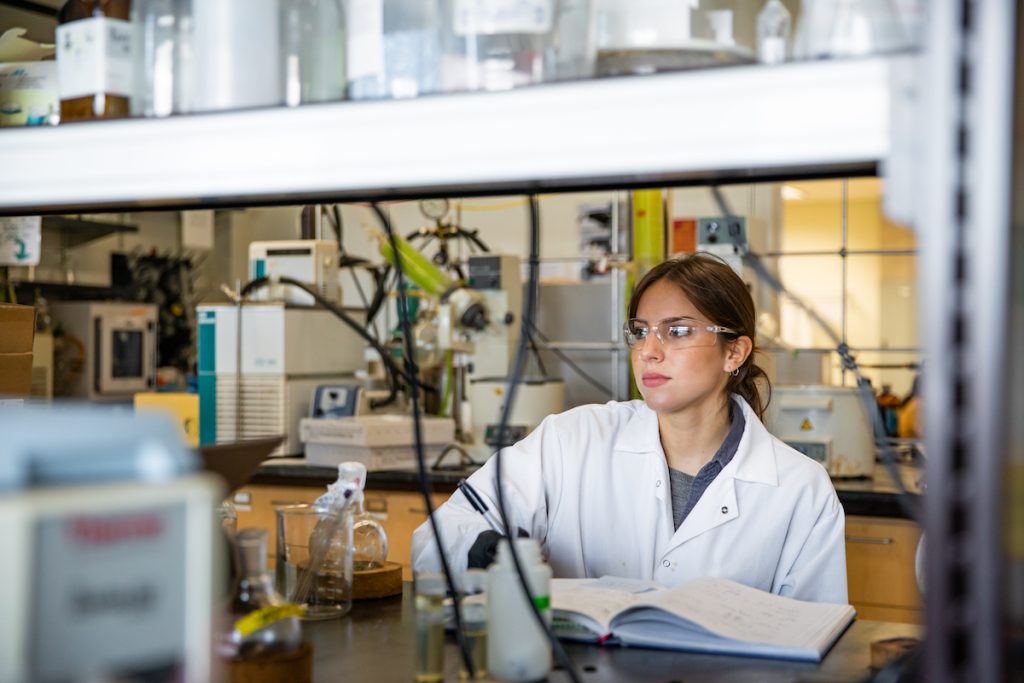Rowan Global student Sarah takes notes while working in a lab.