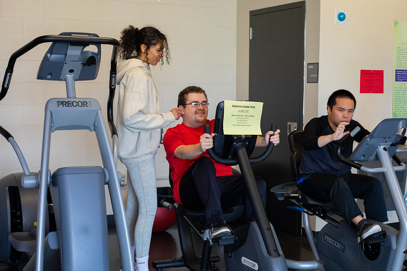 Rowan University Health and Physical Education major Adrianna can be seen at "Get Fit" and is coaching another person how to use a machine.