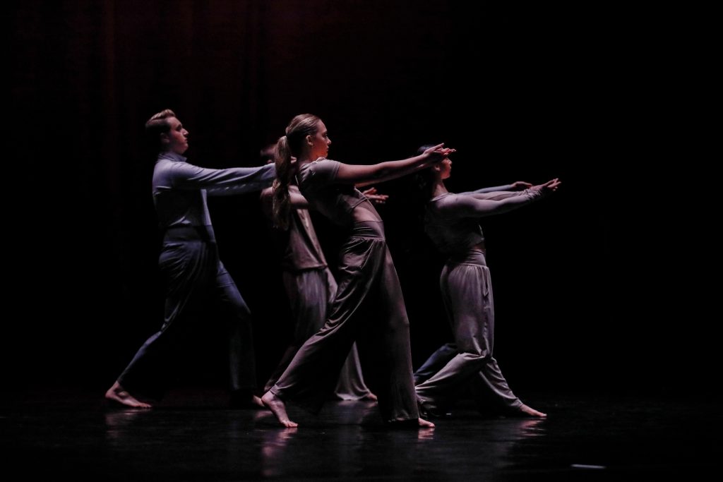 Dancers stand with arms outstretched to the left.