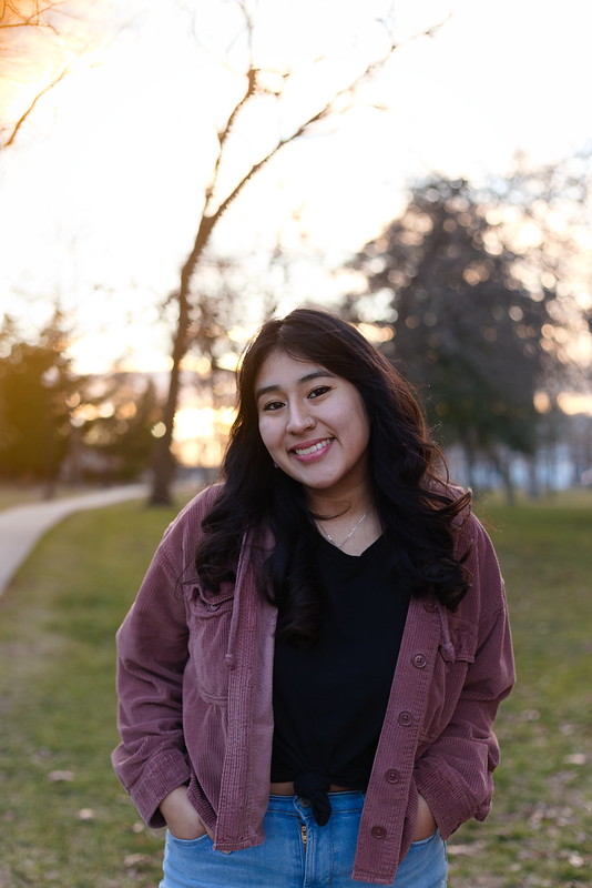 Kathleen is standing with her hands in her pocket smiling brightly. 