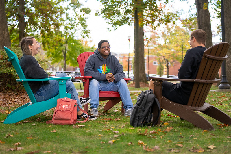 Sedrick is with friends, sitting on one of the lawn chairs on campus. 