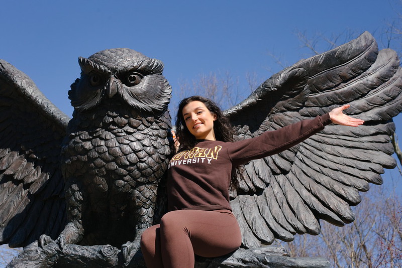 Rowan University Psychology major Siena stands next to the owl statue on campus.