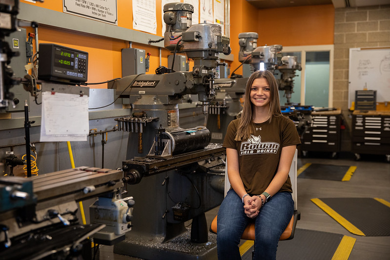 Rowan mechanical engineering student Abby sits in an engineering lab surrounded by equipment. 