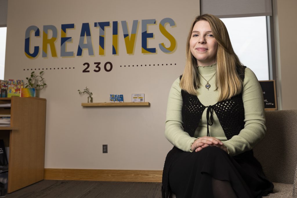 Isabella Shainline posing in front of the yellow & blue Creatives 230 sign.