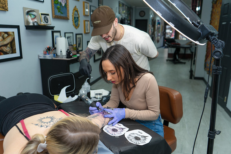 Rowan University studio art graduate Paige Buza tattoos intently with her mentor watching over her shoulder. 