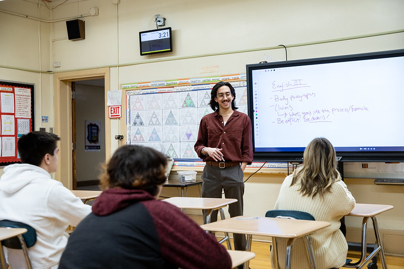 Lucas is standing in front a classroom, talking with students. 