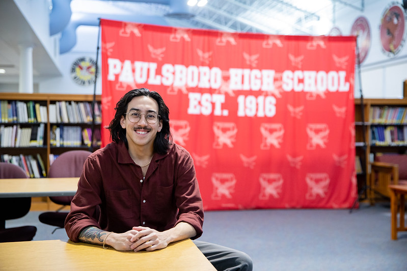 Lucas is sitting at a desk with a large Paulsboro decoration in the back. 