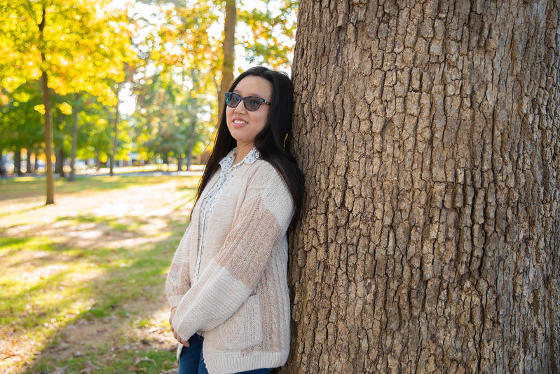 Suzie is leaning on a tree and smiling profoundly. 