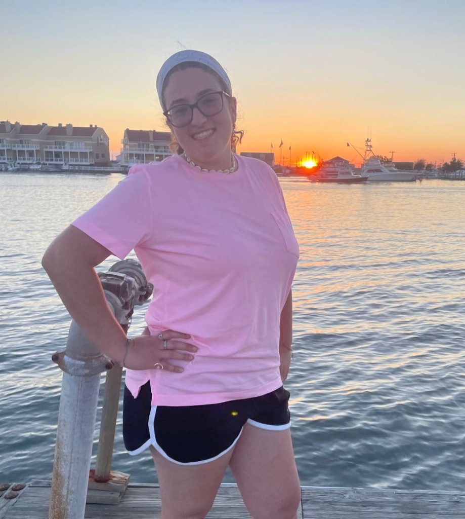 Shannon Russo poses with her hand on her hip, in front of a water sunset.