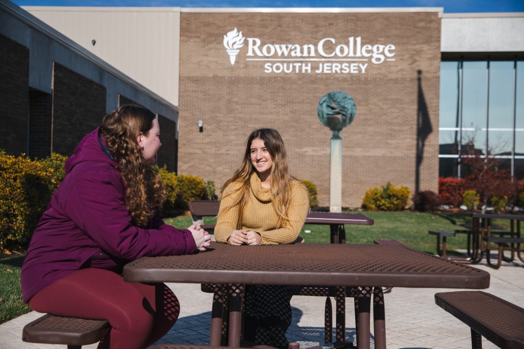 Two students sitting outside the Rowan College of South Jersey entrance.