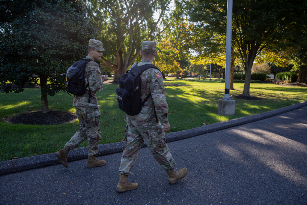Two military students walking outside with their black backpacks.