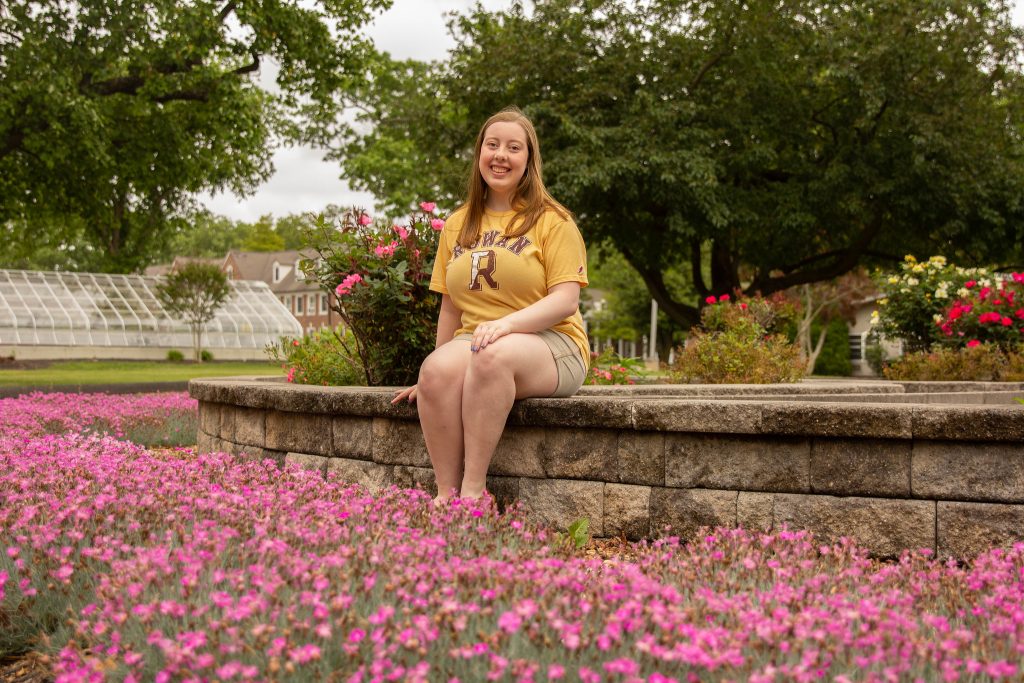 Paige sits formally on a rock ledge with pink flowers around her. 