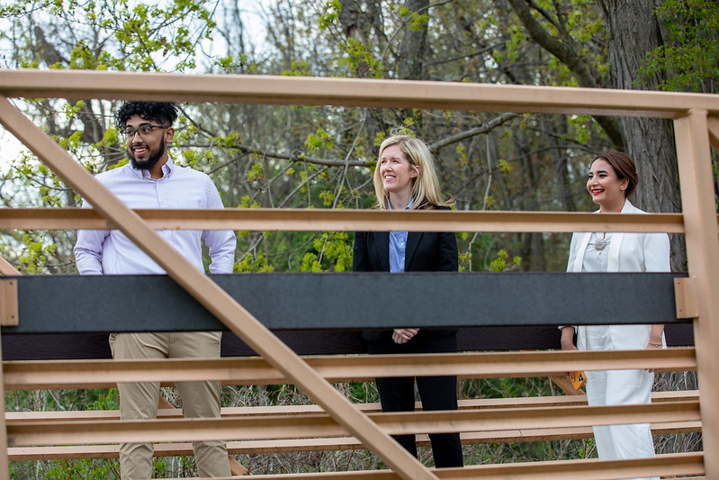 Adult learners dressed in business clothes cross a bridge on campus as they walk together. 