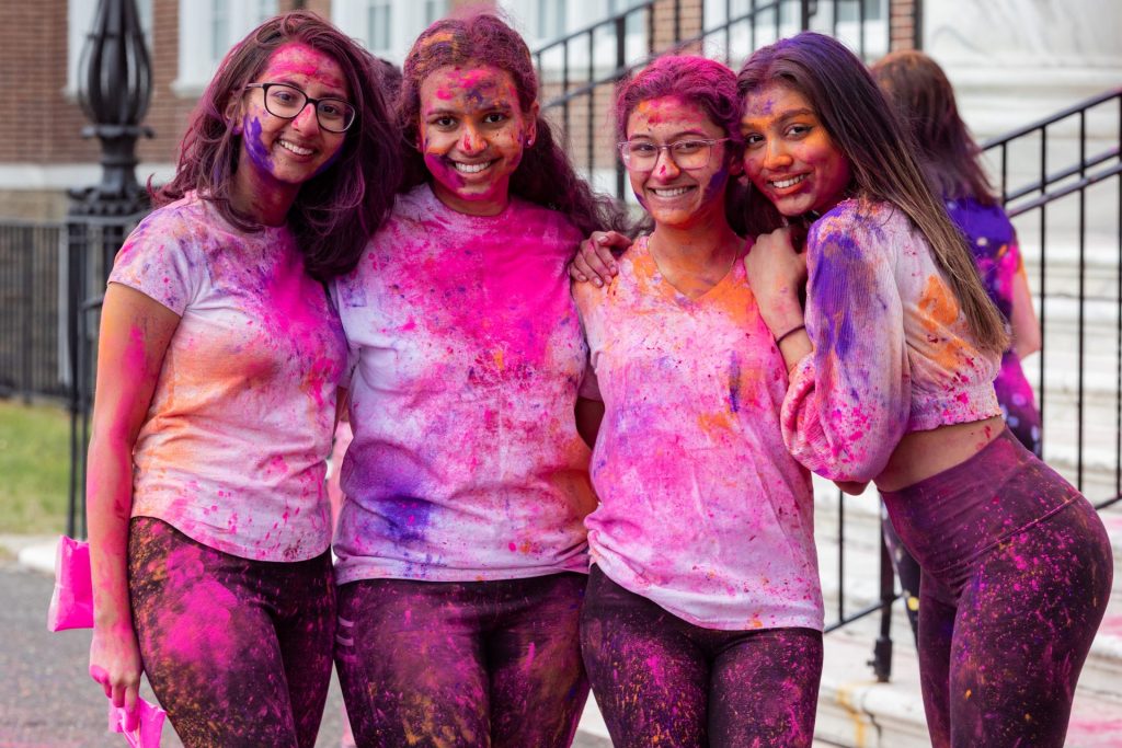 Four friends with purple and pink paint on their bodies hugging eachother.