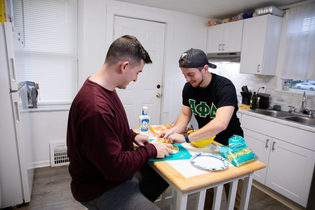 Two Rowan University students prepare a meal in a home kitchen. 