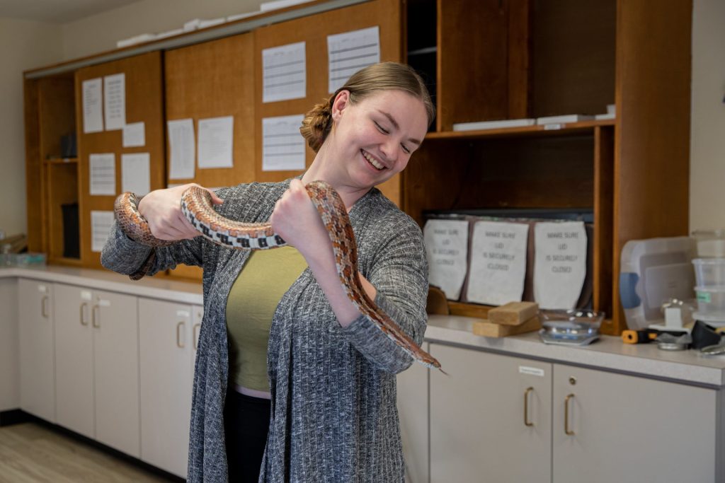 A girl at Rowan University holds a snake and smiles while looking down at it. 