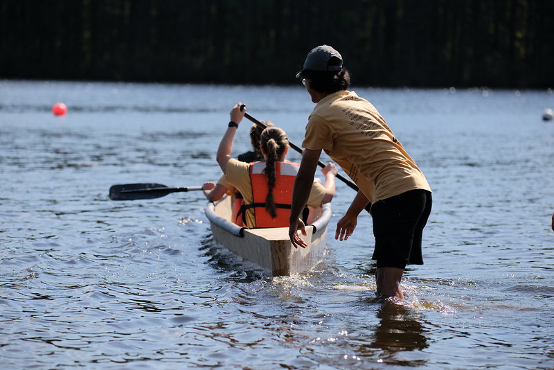 A person pushes the canoe into the water, as two students row. 