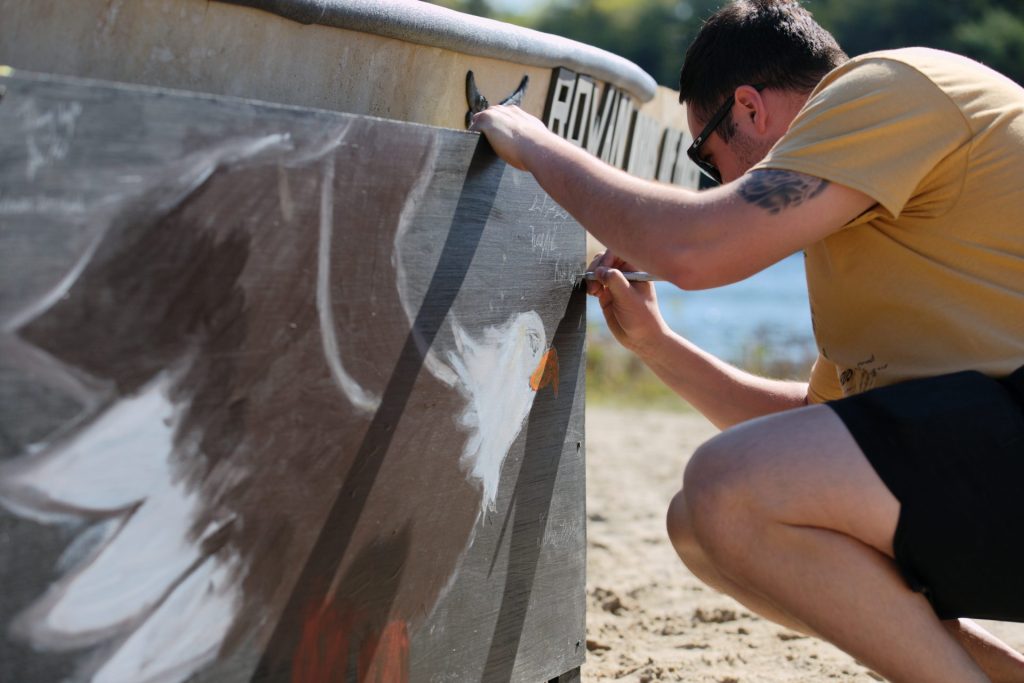 A student writes on the side of the Rowan concrete canoe. 
