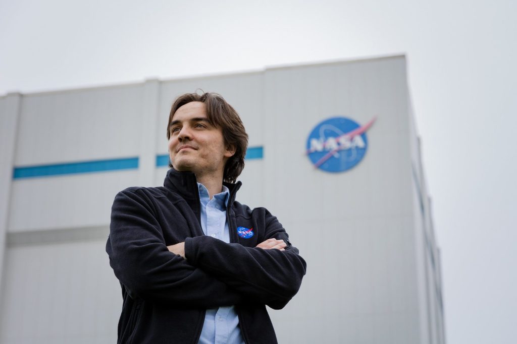 A Rowan University student intern at NASA standing with his arms folded across his chest with the NASA building behind him. 