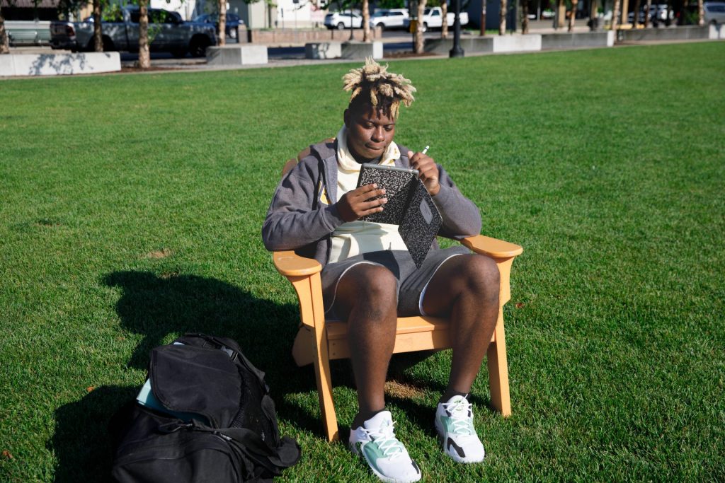 Richard writes in his notebook sitting outside on a chair. 