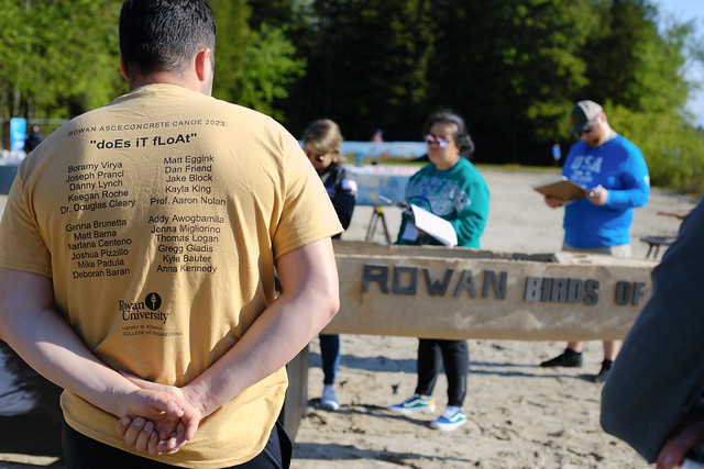A student stands with hands clasped behind his back, watching the Rowan crew carry their concrete canoe. 