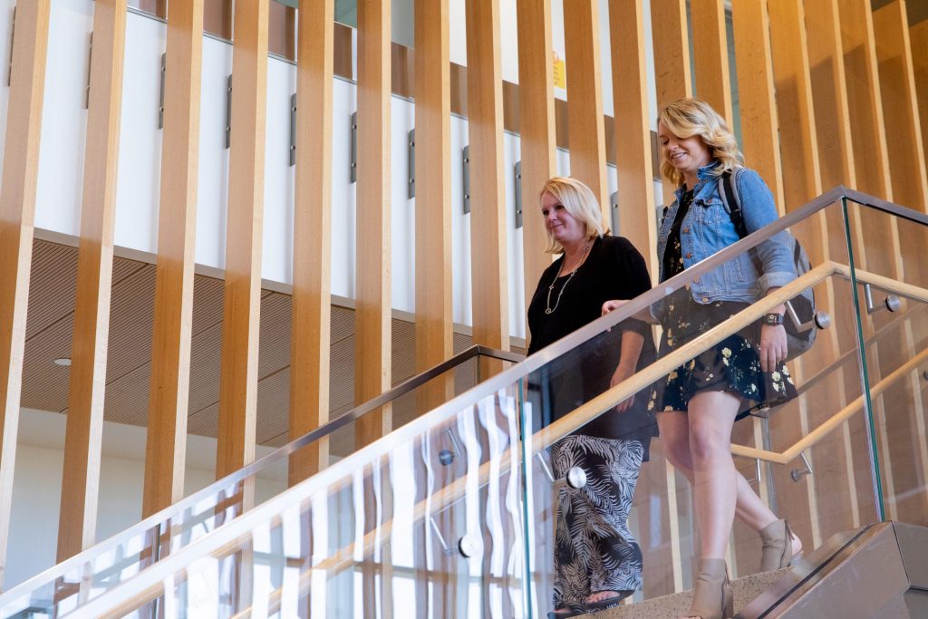 Kellie Stout walking down the stairs inside of the Rohrer College of Business with a fellow colleague.
