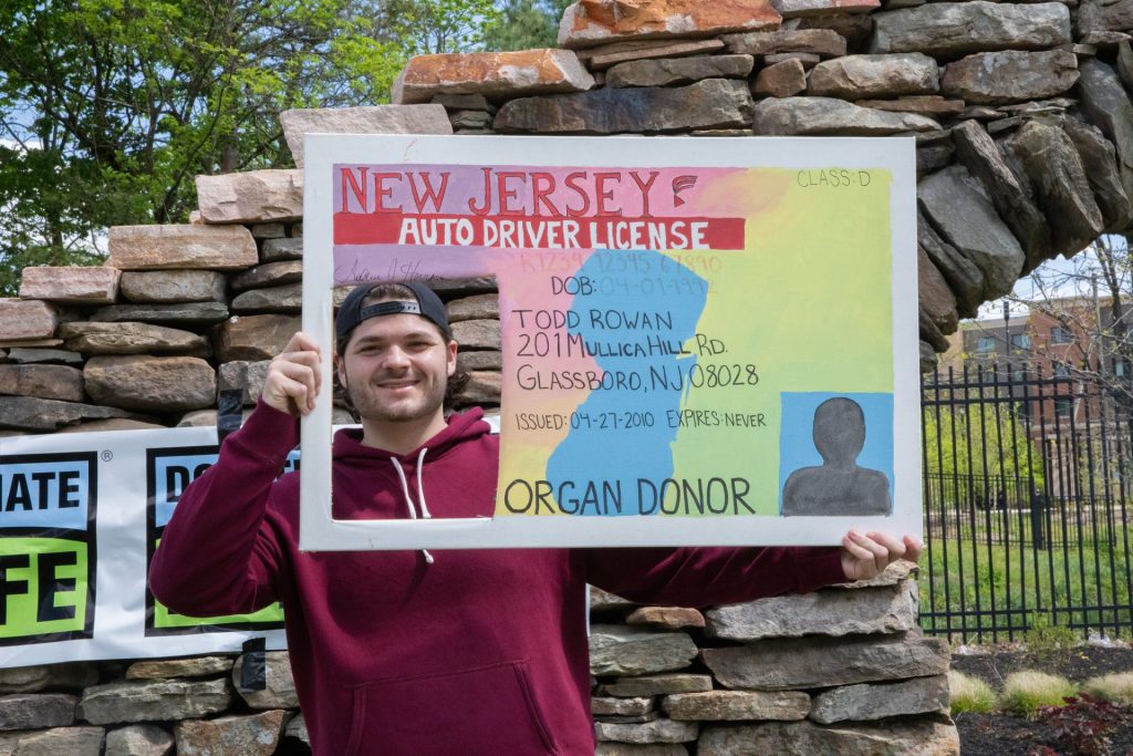 A male PRSSA student poses for a photo with a life-size New Jersey driver's license, with his head in the cardboard cutout, to show he has signed up to be an organ donor. 