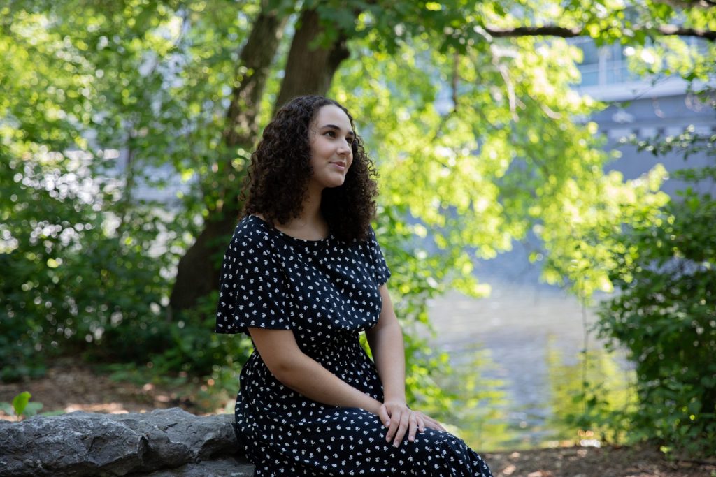 Nina Pantaleone sitting on a rock with a tree and a lake behind her.