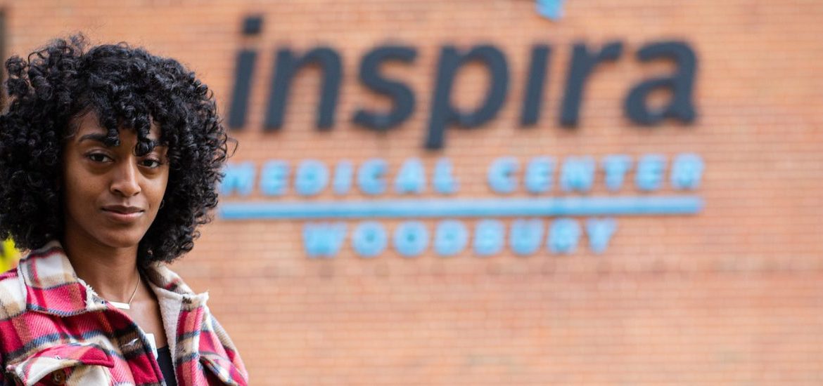 Theresa Bennett stands outside her internship at Inspira Health Network with their logo behind her.