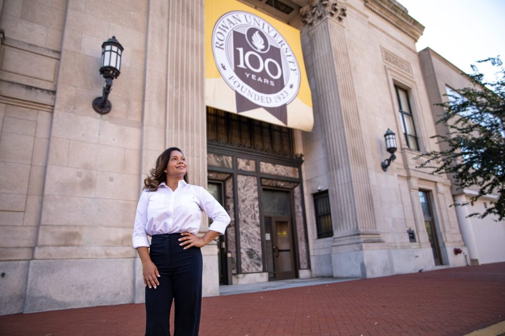Jeanette standing proudly outside a building with a "Rowan 100" banner draped overhead. 