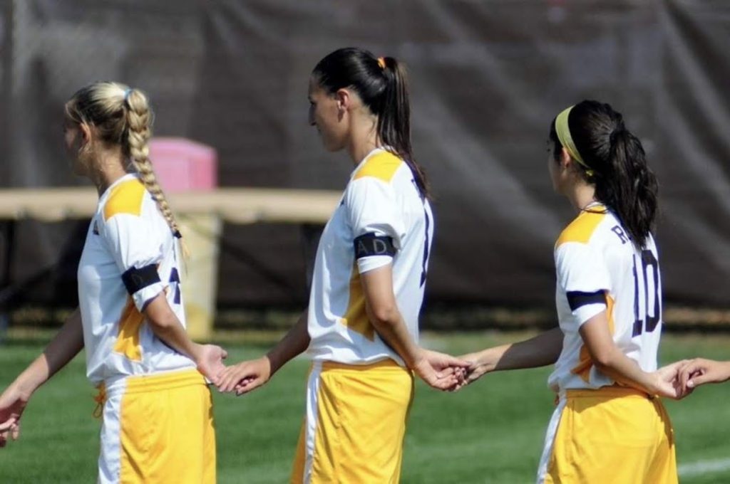 Miranda walks in a line with other soccer players, each holding the hand of the person in front of them and behind them. 